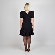 Load image into Gallery viewer, Back view of model in Femponiq Black Pleated Shoulder Peplum Hem Cady Dress, emphasizing the structured fit and elegant V neck closure at the back.