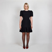 Load image into Gallery viewer, Model wearing the Femponiq Black Pleated Shoulder Peplum Hem Cady Dress, highlighting the sophisticated pleated shoulder detail and the flattering, feminine peplum hem. The dress enhances an hourglass figure with its sculpted silhouette, offering a timeless and elegant design.