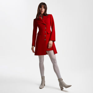 Full-length view of a model wearing the Femponiq Asymmetric Pleated Blazer Dress in red, featuring an asymmetric double-breasted closure, wide peak collar, hand-crafted flower-motif buttons, and padded shoulders. The tailored A-line silhouette includes soft front and rear pleats and a subtle front slit, creating a refined, confident look.
