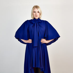 Close-up front view of the Femponiq Bow Tie Neck Cape Sleeve Maxi Dress in Royal Blue, showcasing its elegant bow tie neckline, flowing cape sleeves, and floor-length silhouette.

