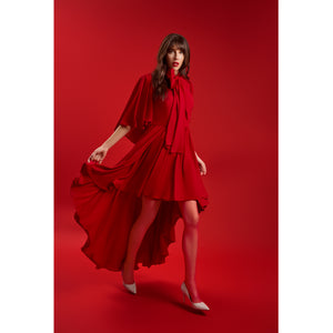 Model wearing the Femponiq Red Bow Tie Neck Cape Maxi Dress, showcasing its flowing cape sleeves and high–low layered hem in motion for a dramatic, feminine look.