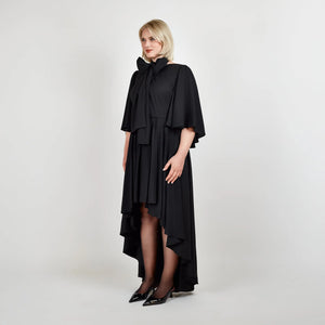 Side view of the Femponiq Bow Tie Neck Cape Sleeve Maxi Dress in Black showcasing its elegant bow tie neckline, flowing cape sleeves, and floor-length silhouette.
