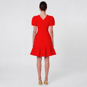 Woman facing backward wearing a bold red fitted midi dress with structured puff sleeves, a cinched waist, and a flared ruffle hem. Styled with gold pointed heels and minimal gold jewelry against a light gray background. Elegant feminine silhouette by Femponiq.