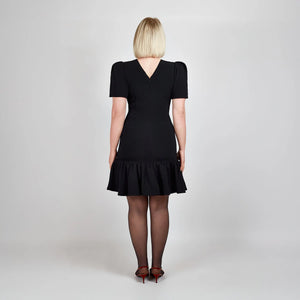 Back view of model in Femponiq Black Pleated Shoulder Peplum Hem Cady Dress, emphasizing the structured fit and elegant V neck closure at the back.
