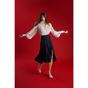 Model wearing the Femponiq High-Waisted Pleated Midi Skirt with asymmetric slits in navy, showing the front movement and elegant flow while walking on a red background.