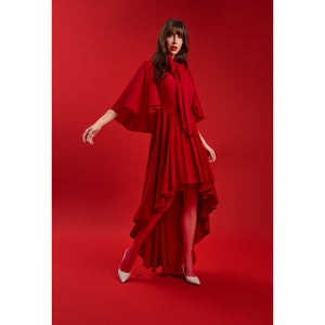 Model wearing the Femponiq Red Bow Tie Neck Cape Maxi Dress, featuring dramatic cape sleeves, an oversized bow neckline, and a high–low cascading hem for a luxurious, feminine silhouette.
