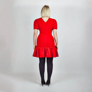 Back view of model in Femponiq Red Pleated Shoulder Peplum Hem Cady Dress, emphasizing the structured fit and elegant V neck closure at the back.