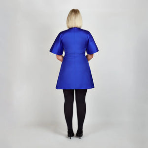 Back view of model in Femponiq Royal Blue Pleated Shoulder Kimono Sleeve Satin Duchess Dress, emphasizing the smooth satin finish and  flared structured skirt and sleeves.