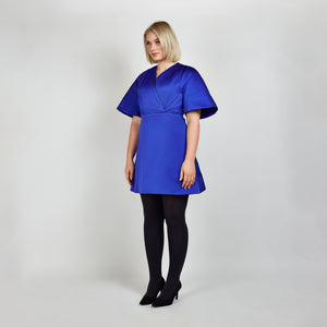 Side view of model in Femponiq Royal Blue Pleated Shoulder Kimono Sleeve Satin Duchess Dress, highlighting the graceful pleated shoulders and the flattering flared 
silhouette.