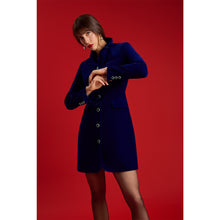 Load image into Gallery viewer, Model wearing a royal blue velvet blazer dress with jewel-embellished buttons, long sleeves, and a fitted hourglass silhouette, standing against a red background.
