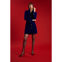 Load image into Gallery viewer, Model wearing the Femponiq Velvet Tailored Royal Blue Blazer Dress, featuring handcrafted sparkling buttons, peak lapels, and an hourglass silhouette, standing against a red backdrop.
