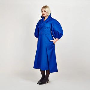 Side view of Femponiq’s Wide Lapel Asymmetric Belted Midi Cotton Dress in a vibrant blue hue, showcasing the stylish wide lapels, asymmetrical hemline, side slit pockets and flattering belt that accentuates the waist.