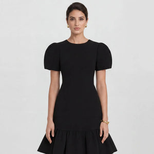 Close-up of the Femponiq Black Pleated Shoulder Peplum Hem Cady Dress in black, highlighting the pleated shoulder detail and luxurious fabric texture.  Showcasing a woman accentuating an hourglass shape with its bold silhouette.