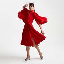 Load image into Gallery viewer, Full-length view of the Femponiq Gathered Midi Red Bow Tie Neck Dress, featuring dramatic draped full-circle sleeves, a bow tie neckline, and a gathered waist. The mid-length pleated skirt includes two front slits that enhance movement, while the fluid fabric creates an elegant, cascading silhouette.
