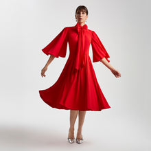 Load image into Gallery viewer, Front view of the Femponiq Gathered Midi Red Bow Tie Neck Dress, featuring dramatic full-circle sleeves, a bow tie neckline, and a flowing mid-length pleated skirt. The soft fabric and subtle front slits create graceful movement and a refined feminine silhouette.
