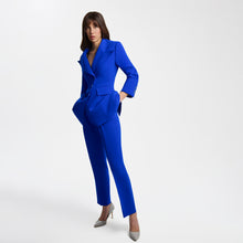 Load image into Gallery viewer, Full-length view of a model wearing bright blue high-waisted tailored trousers with pressed front pleats, paired with a matching structured blazer. The Femponiq trousers feature a sleek long-leg silhouette, functional belt, concealed snap fastening, and slash pockets, creating a polished and modern look.
