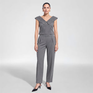 A woman modelling Femponiq's grey sleeveless jumpsuit with a structured V-neckline, wide shoulder panels, a matching belt at the waist, and straight-leg pants, paired with black pointed heels against a light grey studio background.