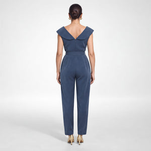 Back view of a model wearing Femponiq’s denim blue vegan cupro jumpsuit, showing the wide folded V-back collar, centre-back zip, belted waist and tapered legs.