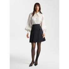 Load image into Gallery viewer, Full-length view of a model wearing Femponiq pearl-white gathered-neck blouse with voluminous sleeves paired with a black pleated silk-blend flared mini skirt. The skirt features a clean A-line shape and front pleat detailing, creating a polished and feminine silhouette.
