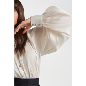 Close-up detail of the pearl-white gathered raglan sleeve on a voluminous blouse, showing the soft sheen of the semi-sheer fabric and the sparkling metal cuff buttons. The elegant drape highlights the feminine, sculptural silhouette.