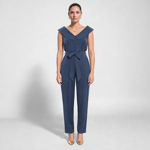 Model wearing Femponiq’s denim blue vegan cupro jumpsuit with a wide folded off-shoulder collar, self-tie waist belt and tapered legs, front view.