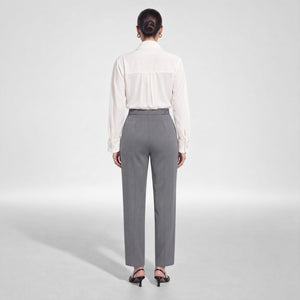 Back view of a model wearing Femponiq’s ivory viscose rayon shirt with gathered back detailing, tucked into charcoal grey cupro-blend trousers with a partially elasticated waistband.