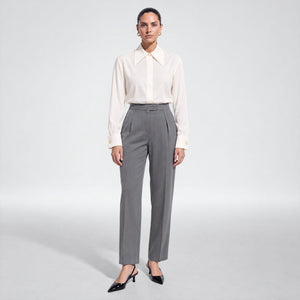 Front view of a model wearing Femponiq’s ivory viscose rayon shirt tucked into high-waisted grey cupro-blend pleated trousers, styled with black slingback heels.