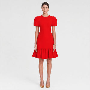 Woman facing forward wearing a bold red fitted midi dress with structured puff sleeves, a cinched waist, and a flared ruffle hem. Styled with gold pointed heels and minimal gold jewelry against a light gray background. Elegant feminine silhouette by Femponiq.