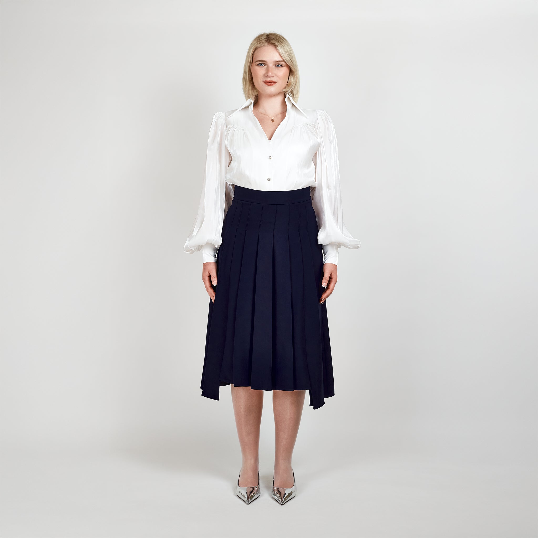 Video of a model wearing the Femponiq High-Waisted Navy Pleated Midi Skirt with Asymmetric Slits and Sheer White Puff Sleeve V-Neck Gathered Shirt, showcasing elegance and movement.